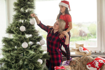有吸引力的妈妈。女儿穿冬天服装装修圣诞节树首页快乐准备庆祝圣诞节节日概念家庭圣诞节聚会，派对