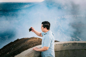 旅游男人。采取照片的观点年轻的旅游男人。采取照片火山的观点喜欢冒险的男人。细胞电话采取照片的观点