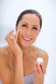 保持皮肤伟大的有吸引力的成熟的女人应用保湿霜皮肤
