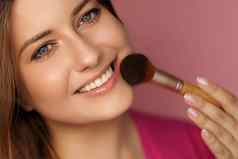 美丽的年轻的女人应用化妆品粉产品化妆竹子刷美化妆护肤品化妆品模型脸肖像粉红色的背景