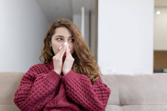 年轻的女人生病的首页流鼻涕的鼻子湿巾鼻子纸手帕坐在沙发上