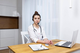 肖像年轻的女医生坐着表格首页工作在线移动PC文档耳机麦克风白色外套