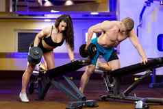 年轻的体育健身教练男人。火车年轻的美丽的女人运动员健身房显示练习哑铃肱二头肌腿