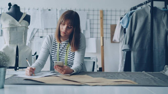 有创意的服装设计师智能手机画草图工作现代裁缝商店缝纫表格女人忙涉及到过程