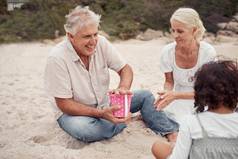 快乐沙子爷爷奶奶玩孙子海滩夏天积极的上了年纪的男人。女人建筑沙塔孙子海洋家庭假期
