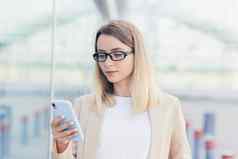 肖像业务女人眼镜金发女郎读取新闻移动电话应用程序重写消息