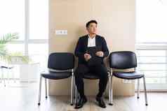 年轻的成功的亚洲男人。等待工作面试等待房间办公室中心坐着椅子接待办公室中心
