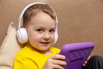 快乐男孩黄色的衬衫玩游戏数字平板电脑首页肖像孩子首页看卡通紫罗兰色的平板电脑现代孩子教育技术