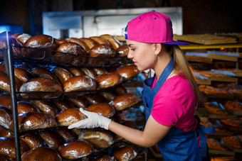 年轻的女孩作品面包店把面包架子上女人贝克工作场所面包店专业贝克持有面包手面包生产概念