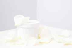 白色Jar奶油精致的白色玫瑰花花瓣光背景自然有机化妆品概念关闭模型
