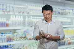 亚洲买家超市乳制品部门男人。选择牛奶读取标签