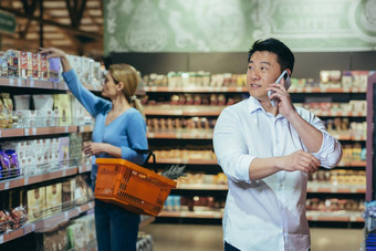 亚洲男人。超市使购买选择产品会谈电话咨询妻子购物列表