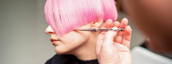 手理发师切割短粉红色的剪刀头发美容沙龙关闭一边视图