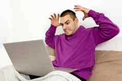 愤怒的不满意男人。紫罗兰色的连帽衫坐着床上移动PC电脑男人。笔记本冲浪互联网读新闻看电影研究工作在线负情绪压力