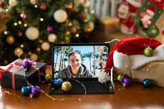 微笑英俊的年轻的男人。享受装修圣诞节树持有平板电脑视频调用自拍首页庆祝一年