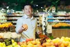 亚洲男人。购物超市站水果蔬菜部分篮子