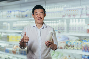 广告肖像年轻的英俊的亚洲男人。超市持有瓶牛奶