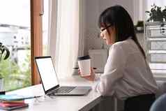 一边视图亚洲女人办公室工人喝咖啡阅读业务电子邮件移动PC电脑