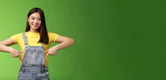 友好的即将离任的可爱的亚洲年轻的女人显示手指介绍促销应用程序微笑快乐分享链接推荐产品品牌咧着嘴笑露出牙齿的绿色背景