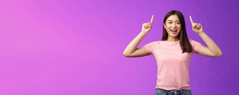 有魅力的好看的活泼的微笑亚洲女孩介绍产品指出手指前广告咧着嘴笑露出牙齿的兴奋告诉好新闻分享链接紫色的背景