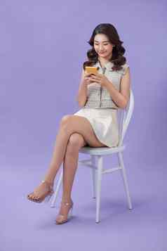 年轻的亚洲女人坐着智能手机紫色的背景