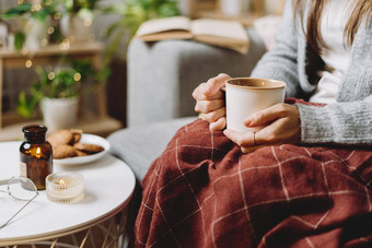 舒适的女人腿针织冬天温暖的毛衣网纹格子喝热可可咖啡杯子坐着沙发上首页秋天共鸣蜡烛装饰饼干室内植物