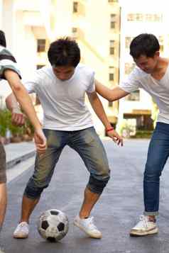 享受学校游戏年轻的亚洲男孩玩足球街