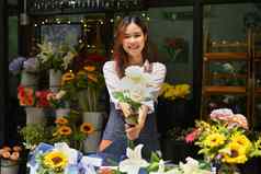 美丽的女围裙持有花束白色玫瑰微笑相机站前面花商店