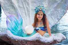 美丽的快乐女孩美人鱼服装坐在大海壳牌