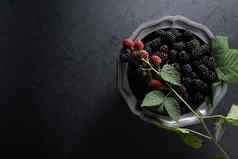完整的板成熟的黑莓用钉子钉上红色的浆果锡碗