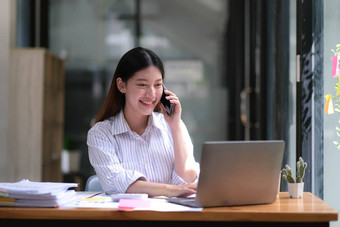 肖像年轻的亚洲业务女人说话智能手机写笔记本移动PC首页办公室美丽的女孩桌子上电脑首页订单启动业务亚洲女人在线锻造电话销售
