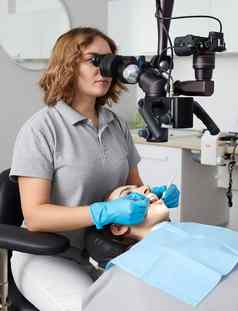 女牙医显微镜治疗病人牙齿牙科诊所办公室医学牙科健康护理概念