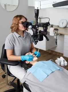 女牙医显微镜治疗病人牙齿牙科诊所办公室医学牙科健康护理概念