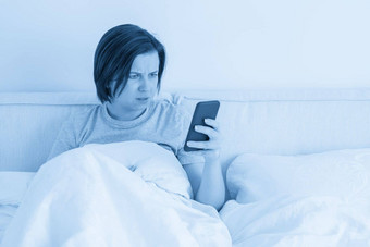 惊讶女人智能手机坐在床上覆盖<strong>羽绒被</strong>