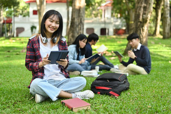 快乐的亚洲女<strong>大学大学</strong>学生数字平板电脑绿色草校园