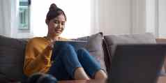 坦诚的亚洲女人平板电脑看在线电影流移动设备沙发生活房间年轻的快乐女孩享受娱乐媒体在线周末