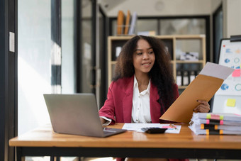 微笑年轻的非洲美国女金融企业家坐着工作场所办公室霍丁咖啡杯工作移动PC投资金融文档报告金融分析概念