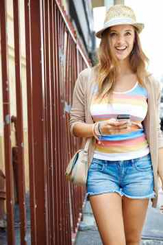 探索周围的环境华丽的年轻的女人穿休闲夏天衣服走城市街发短信手机