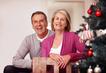 快乐的成熟的夫妇坐着圣诞节树首页肖像快乐的成熟的夫妇坐着圣诞节树首页