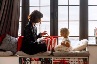 妈妈。女儿坐窗台上持有礼物装饰圣诞节房间妈妈。黑色的睡衣女儿白色衣服一年的家庭假期