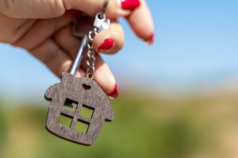 键钥匙链形式房子女人的手背景绿色植物天空概念购买房子公寓真正的房地产年轻的家庭抵押贷款贷款租赁住房