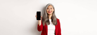 上了年纪的女商人红色的夹克显示空白智能手机屏幕微笑演示移动应用程序白色背景