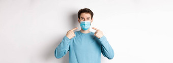 冠状病毒健康检疫概念年轻的高加索人男人。休闲衣服指出医疗面具预防措施流感大流行白色背景