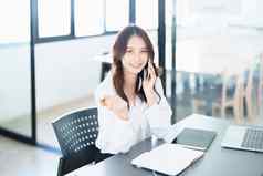 肖像年轻的亚洲女人显示微笑脸电话电脑金融文档桌子上早期早....小时