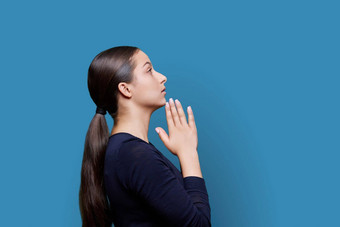 年轻的女恳求持有手祈祷蓝色的背景配置文件视图