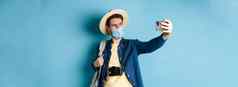 科维德流感大流行旅行概念旅游夏天假期采取自拍医疗面具拍摄智能手机站蓝色的背景
