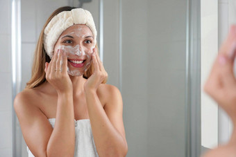 微笑坦诚的女孩洗脸发泡肥皂擦洗皮肤年轻的女人脸洗去死皮擦洗肥皂擦洗护肤品清洗产品