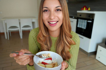 年轻的女人吃牛奶什锦早餐格兰诺拉麦片燕麦片水果酸奶相机厨房