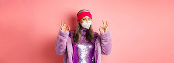 科维德流感大流行时尚概念很酷的亚洲祖母穿时尚的迪斯科衣服呼吸器显示迹象穿脸面具社会距离粉红色的背景