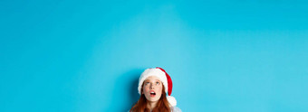 冬天假期圣诞节夏娃概念头漂亮的红色头发的人女孩圣诞老人他底标志促销提供惊讶蓝色的背景